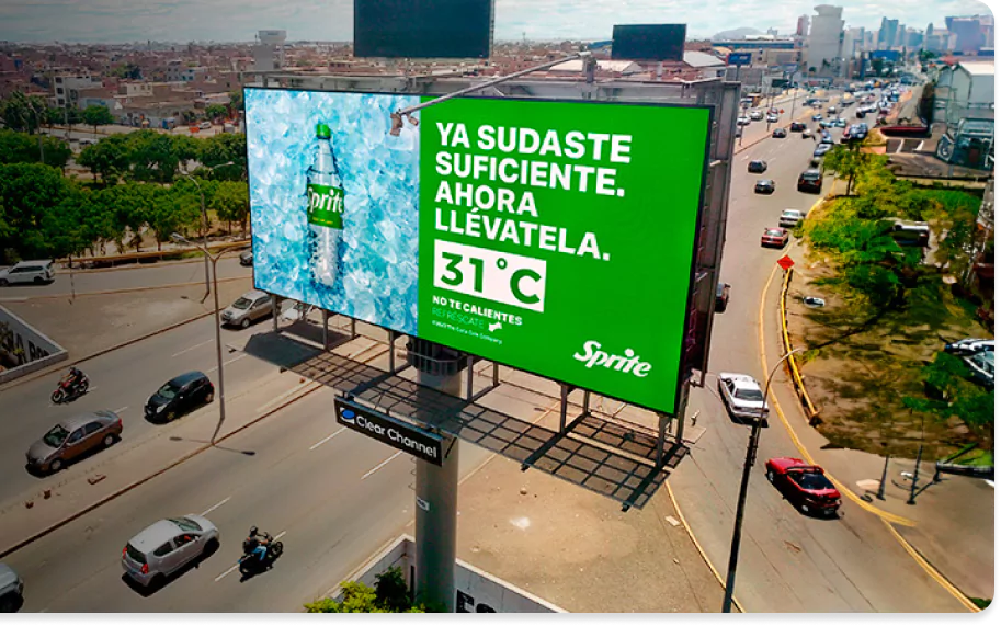 Outdoor da Sprite em uma avenida movimentada, com o slogan 'Ya sudaste suficiente. Ahora llévatela.' em destaque, acompanhado da temperatura de 31°C, convidando os motoristas a se refrescarem Carros e motos transitam pela via ao lado