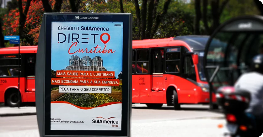 Painel publicitário da SulAmérica em Curitiba promovendo o plano de saúde "Direto Curitiba". A propaganda das empresas destaca benefícios como mais saúde para o curitibano e economia para locais, como o Jardim Botânico de Curitiba ilustrado ao fundo.